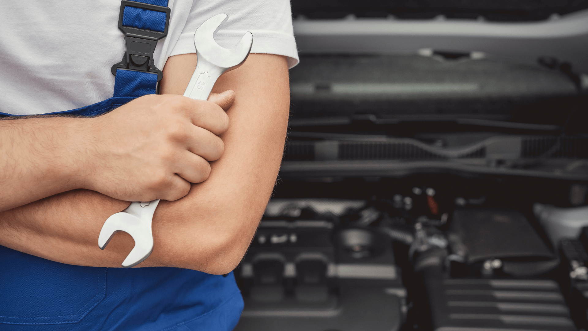 Homme avec une clé a molette devant une voiture capot ouvert